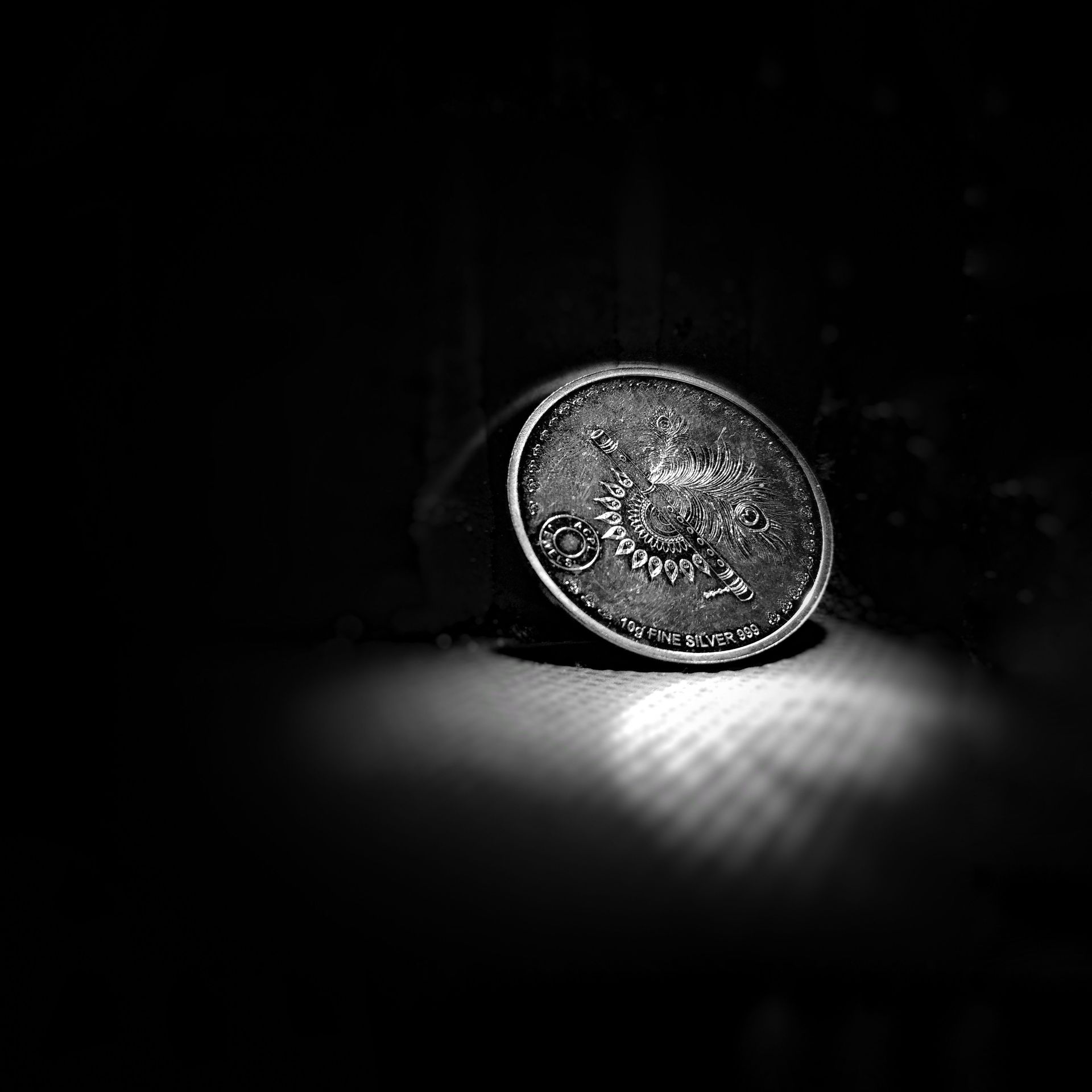 Close-up of a silver coin with detailed patterns on a dark background.