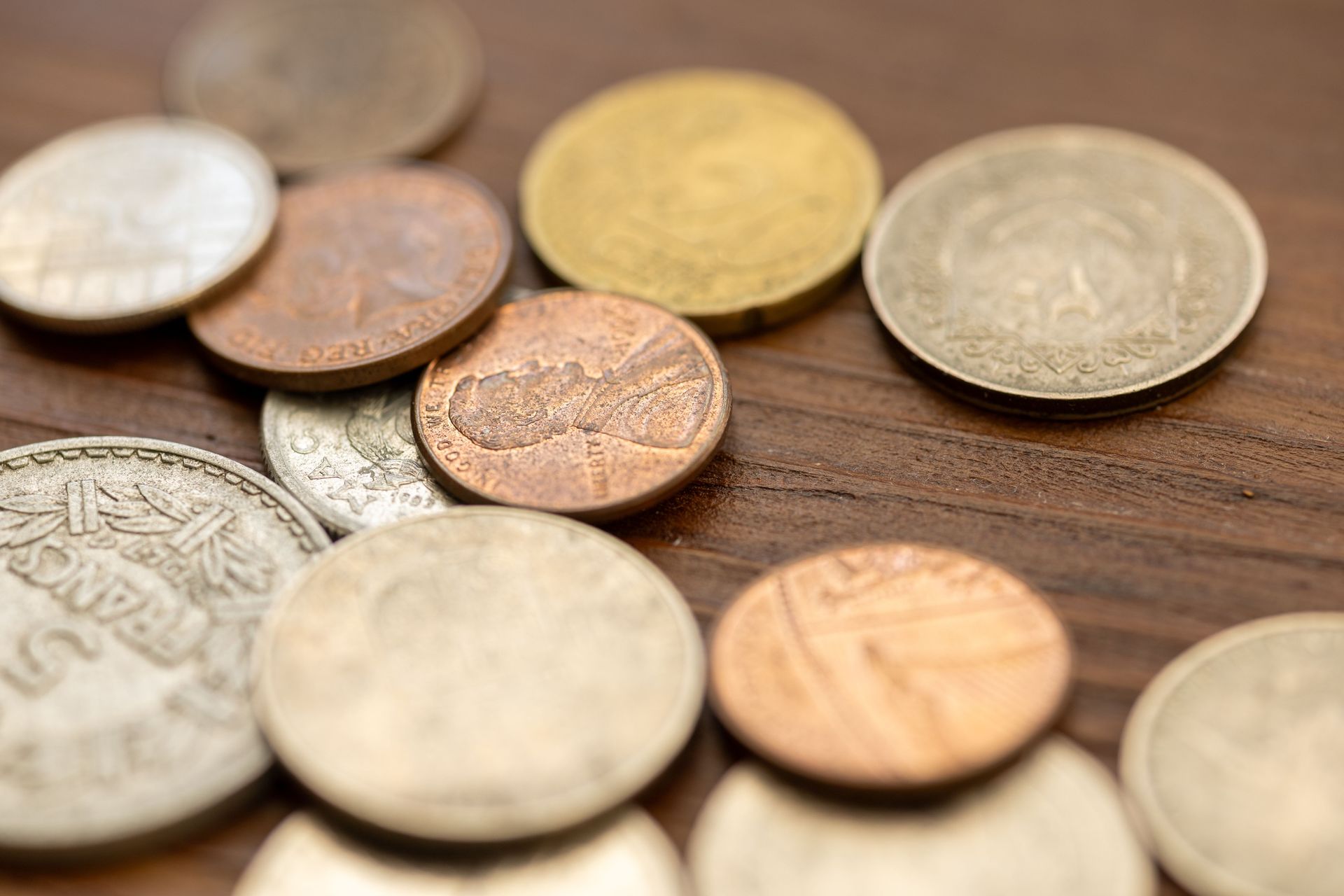 A detailed close-up image showing various vintage coins scattered on a wooden surface, capturing their unique textures and engravings.