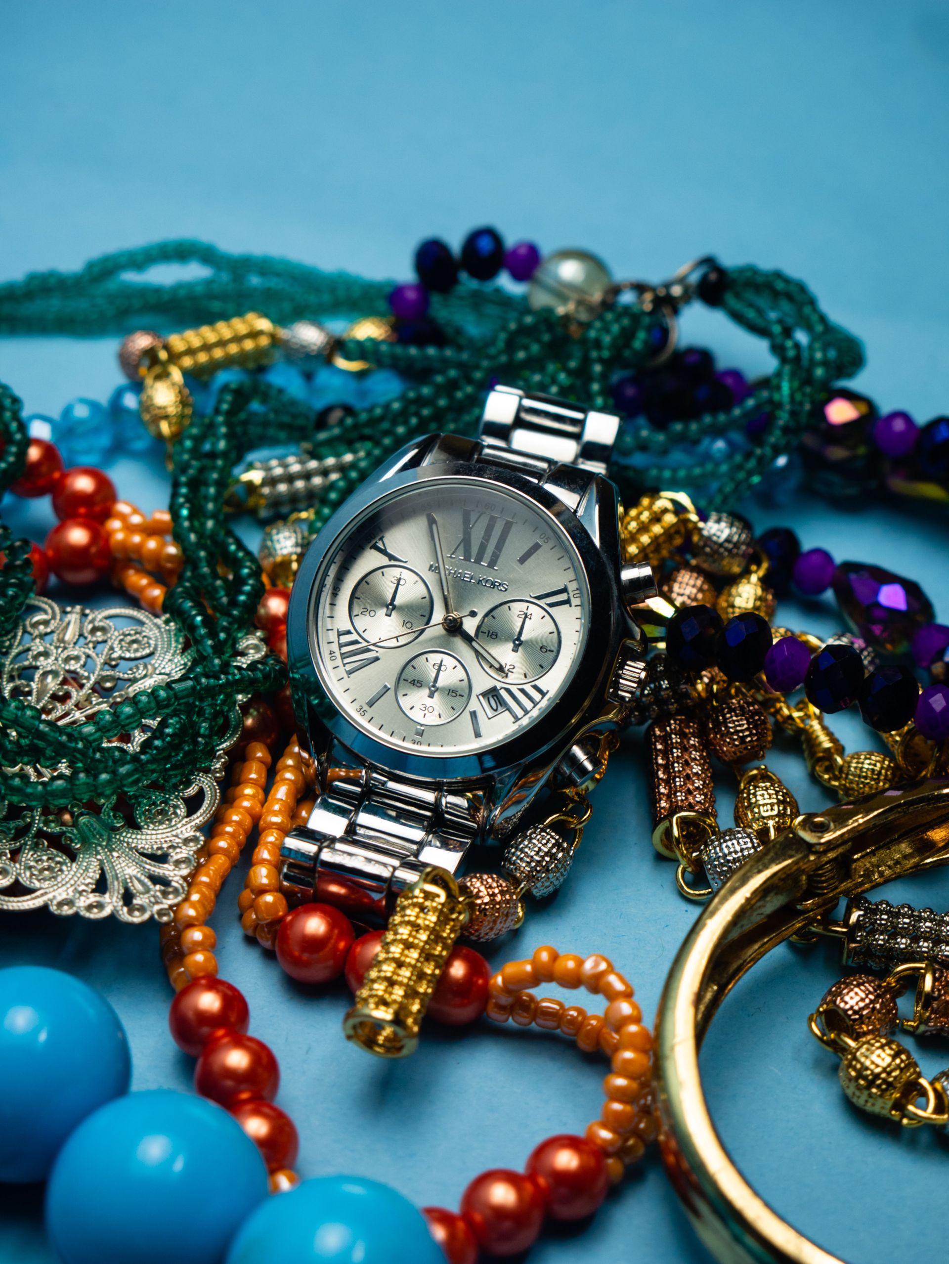 Close-up of elegant wristwatch surrounded by colorful beaded bracelets, showcasing vibrant fashion accessories.